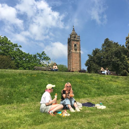 Two people sitting on a grassy hill on a sunny day